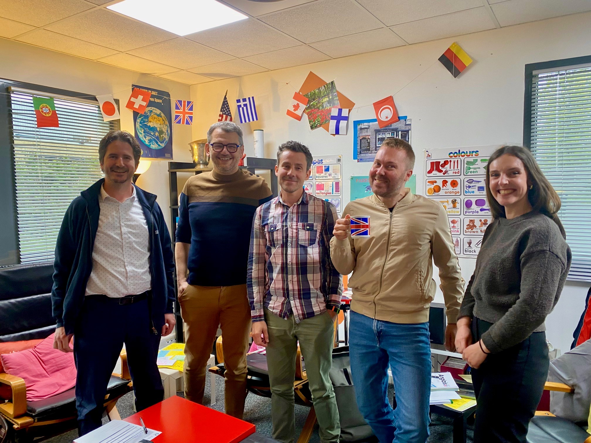 Cinq personnes souriantes dans une salle du centre décorée de drapeaux